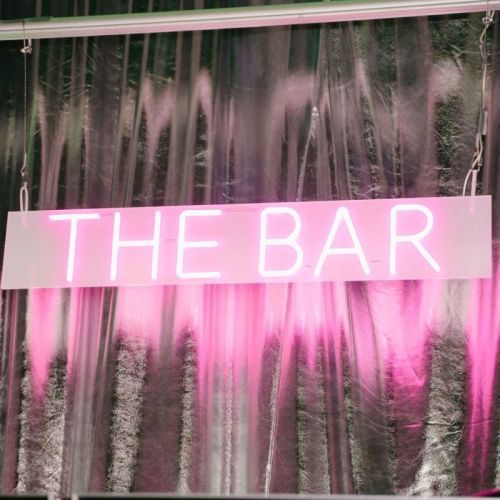the bar neon sign on silver drape